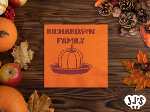 A close-up image of a custom napkin with a pumpkin pie design and personalized text, folded on a table setting.