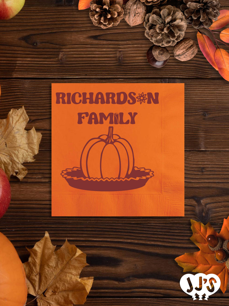 A close-up image of a custom napkin with a pumpkin pie design and personalized text, folded on a table setting.