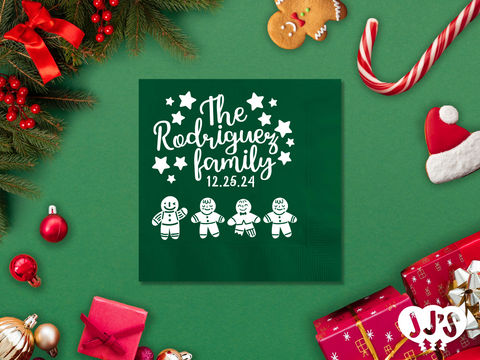 A festive Christmas napkin featuring a gingerbread family enjoying the holiday season, with options to customize with a family name and a custom message.